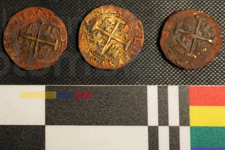 Three very old coins on a table next to some patterned material