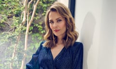 Actor Kat Stewart in a blue blouse leaning against a pale grey wall
