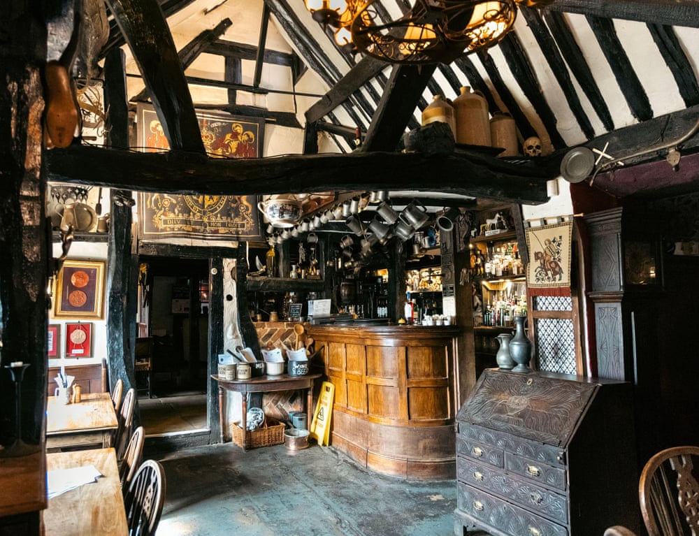 Interior of old pub with timber beams and tankards hanging over bar.