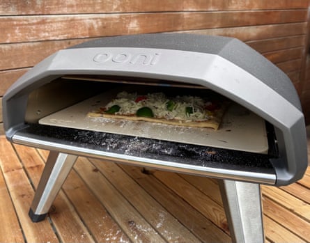 An uncooked vegetable into the Ooni Koda 2 pizza oven, while outdoors on a wooden table.