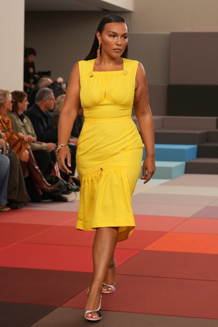 A model who is curvier than the usual catwalk figures wears a tight, bright yellow sleeveless dress with gathered-in waist and a skirt that flares out from below the hips to her knees