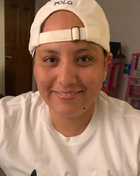 A person smiling, wearing a white baseball cap backwards and a white T-shirt.