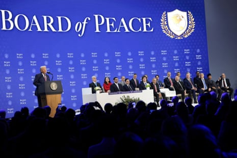 a man speaks into a microphone to a crowd of people while standing in front of a backdrop that says 'board of peace'