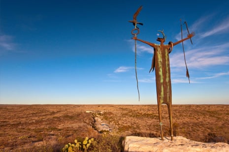A statue of a humanoid-animal figure on a scrubby plain