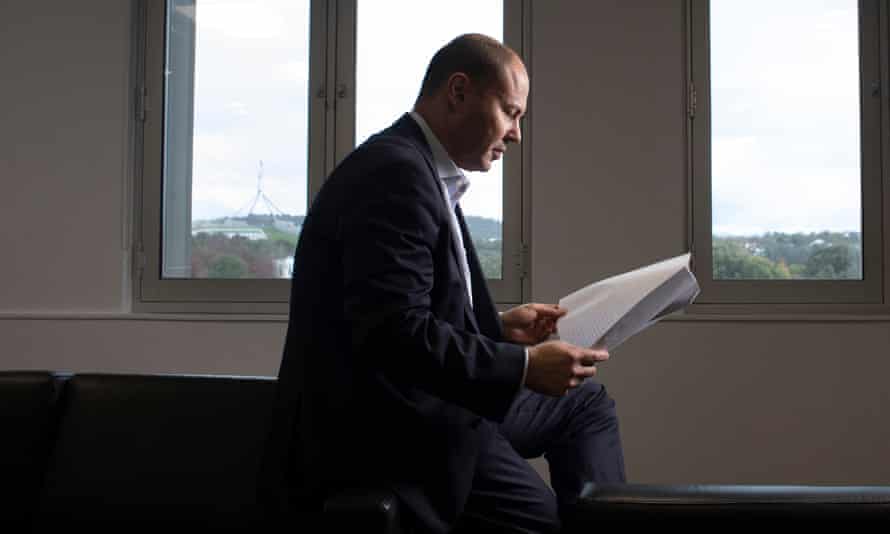 Josh Frydenberg sits reading papers before large windows
