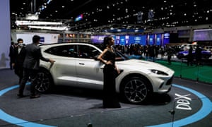 A model wearing a face shield poses with an Aston Martin DBX