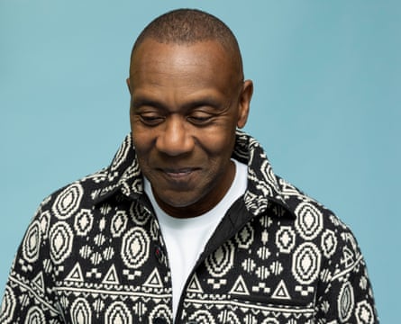 Head shot of Lenny Henry in white T-shirt and back and white jacket, against blue background