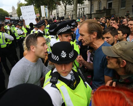 Police officers in high-visibility vests stand between crowds of protesters in an urban street