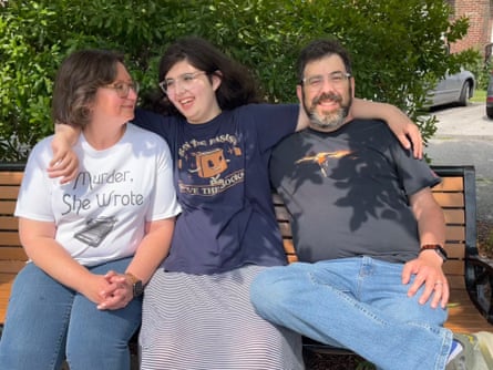 A family of three smile while embracing each other and sitting on a park bench