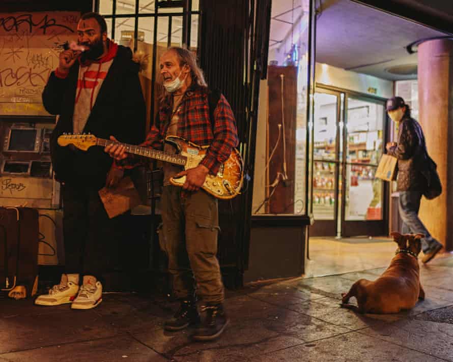 two people stand on street. Myrin holds electric guitar