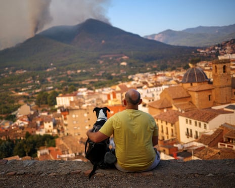 A man and his dog look at a wildfire in a mountain in Onda, Spain.