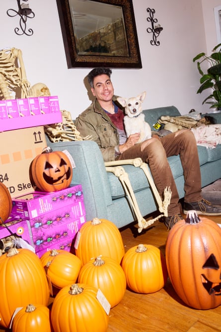 Diego Linares smiles holding his dog on a sofa surrounded by Halloween skeletons and pumpkins