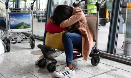 A woman sleeps on a luggage trolley at Heathrow airport.