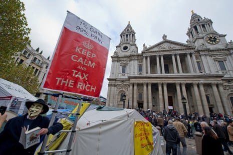 A masked protester holds a sign saying "Keep calm and tax the rich" outside St Paul's cathedral