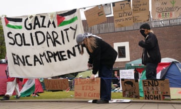 People wearing black clothing and masks with signs reading ‘Gaza solidarity encampment’, ‘15,000+ kids. Do u care?’ and ‘End Israeli investment now’.