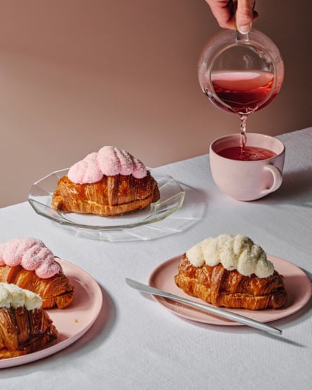 Finger bun croissants, that is, croissants topped with coconut glaze and filled with strawberry jam, arranged on pink plates.