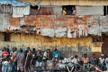 A row of young people sitting and standing outside a corrugated iron building