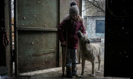 Zlata, 6, pets a dog as she stands at a gate with holes created by shrapnel near her house, in the village of Posad-Pokrovske, Kherson region.