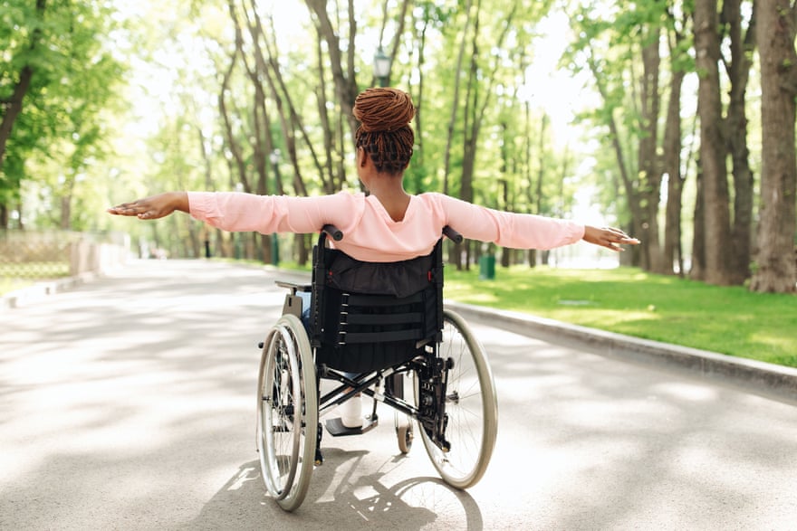 Back view of millennial African American woman in wheelchair going for walk at city park, feeling free outdoors, full length. Young black lady with physical disability enjoying spring nature