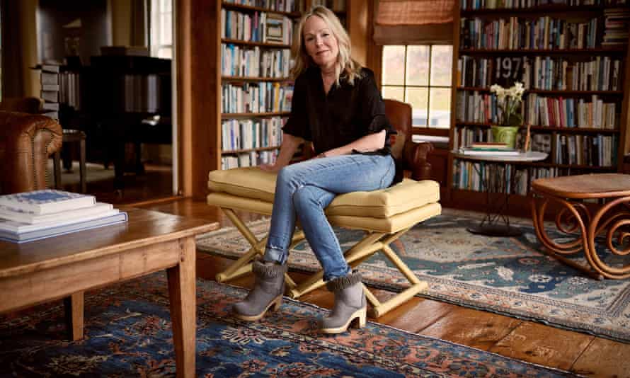 Dani Shapiro, in jeans, a black top and ankle boots, at her home in Connecticut, in her study/library, surrounded by shelves of books and Persian rugs