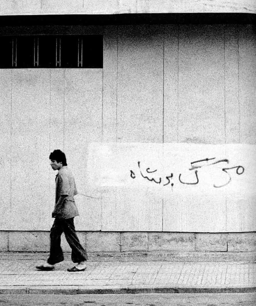 A man walks past a wall with ‘Death to the Shah’ scrawled over what appears to be similar graffiti previously covered up.