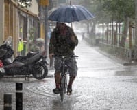 A man rides a bicycle with an umbrella during heavy rain in downtown Barcelona, Spain