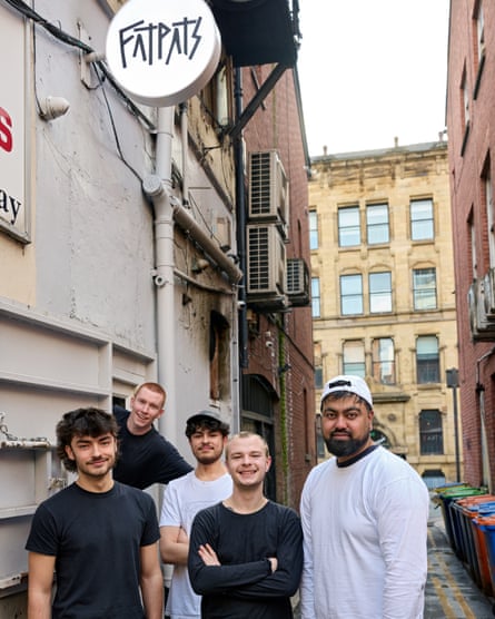 A group of men standing in a lane, with the sign for a restaurant