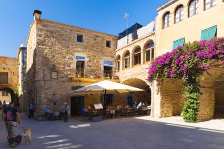 People eating under a large umbrella outside medieval stone buildings on a bright sunny day