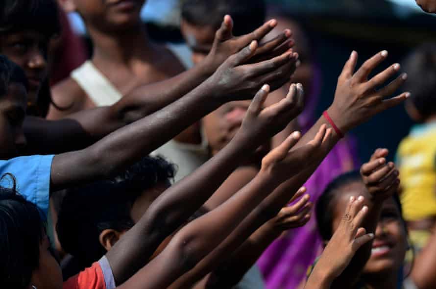 Children raise their hand for biscuit packets, being distributed by volunteers at a hastily-constructed camp in Assam state where more than a million people have lost their homes.