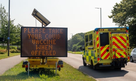 An emergency ambulance passes a large Please Take Your Covid Vaccine When Offered LED roadside sign on the A4.