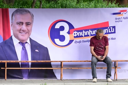 A man sits on a bench next to a campaign poster of Strong Armenia, Samvel Karapetyan’s party.