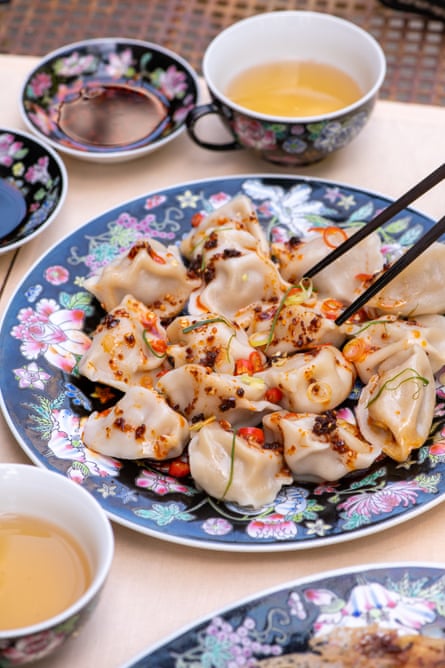 A plate of boiled fish dumplings with a spicy dressing on a floral plate.spicy mackerel, lemon and dill shui jiao.