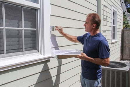 Man painting exterior of house holding paint tray.