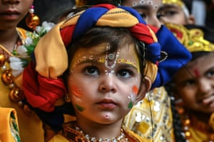 A wearing a red, yellow and white hat and colourful face paints, including the Indian flag colours painted on their cheeks