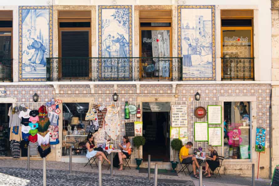 Tourists at a hillside cafe in the Alfama district of Lisbon with a typical tiled facade