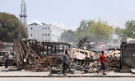 People walk past burnt remains of vehicles near the presidential palace, Port-au-Prince