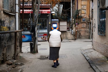 a picture of a street scene shows an optical illusion of older lady with an ATM machine for a head in a photo by Lewis Denby