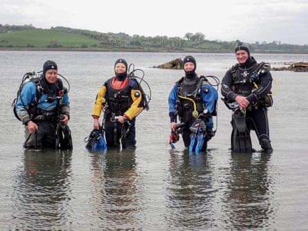 Four people in diving gear standing knee-deep in a lough.