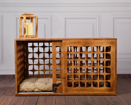 A mid-century style dog crate with dog bedding inside and a candle on top. It’s sitting on a wooden floor and the wall behind is white and panelled