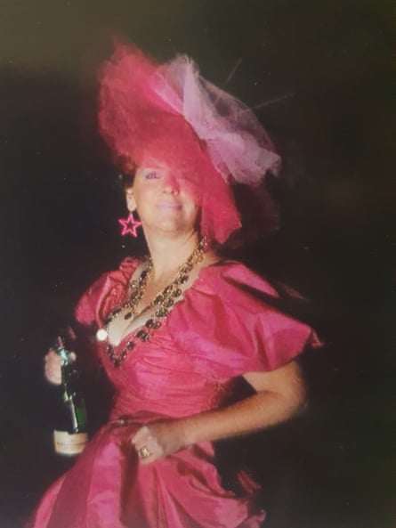 A woman wearing a bright pink dress and matching headdress holding a bottle of bubbly.