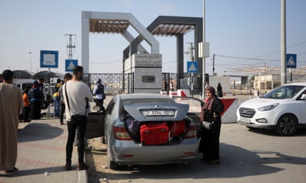 Palestinians stand beside their stationary car, its trunk open to show suitcases crammed inside, in a queue at the border crossing