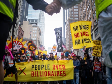 People hold signs that say “no kings” and “people over billionaires”