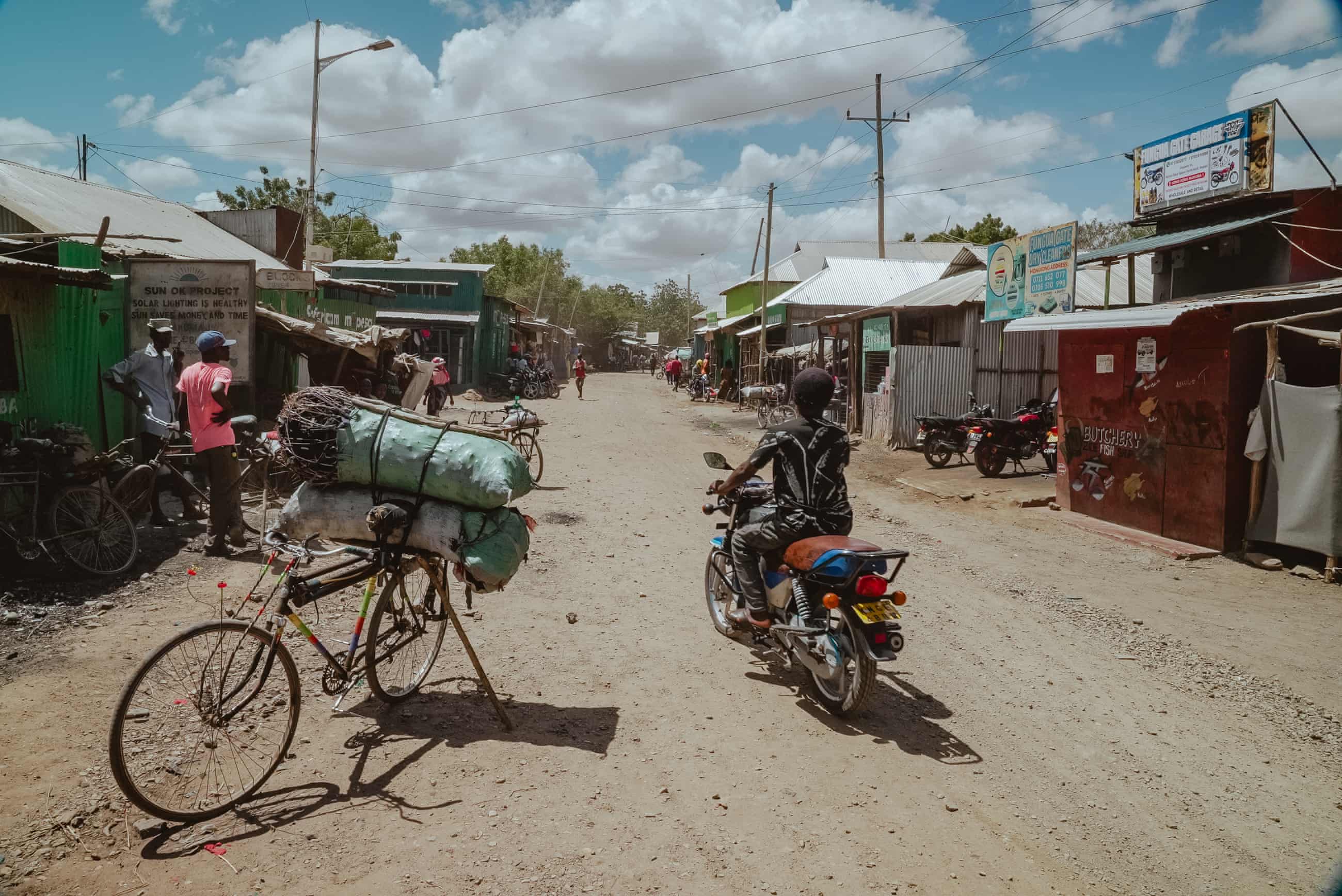 People on bikes ride along a dusty road in a market