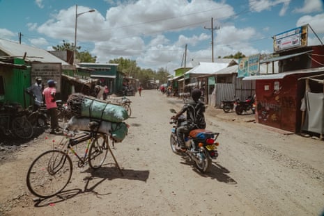 People on bikes ride along a dusty road in a market