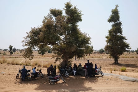 Bello’s gang sit and stand under a tree, some with motorbikes