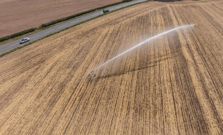 Aerial view of a brown field being watered with a long irrigator spray