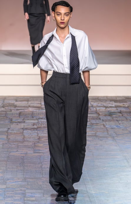 A model wearing a white blouse and grey trousers