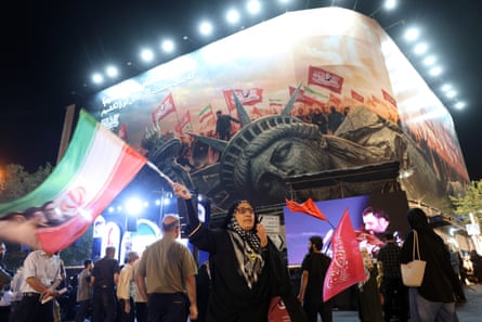 A group of people wave flags at night in front of a large billboard,