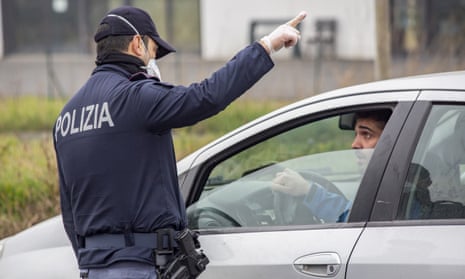 A police officer wearing a protective mask speaks with a motorist at a yellow zone quarantine roadblock, near the red zone in the town of Codogno