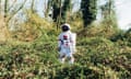 Young astronaut wearing space suit and helmet, standing in bush